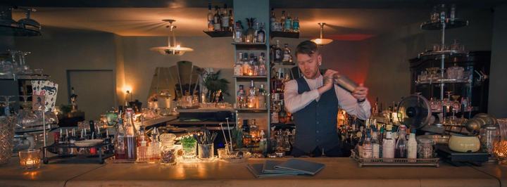 Le Verre à Monique, Geneva: bartender shaking a cocktail behind the candlelit bar